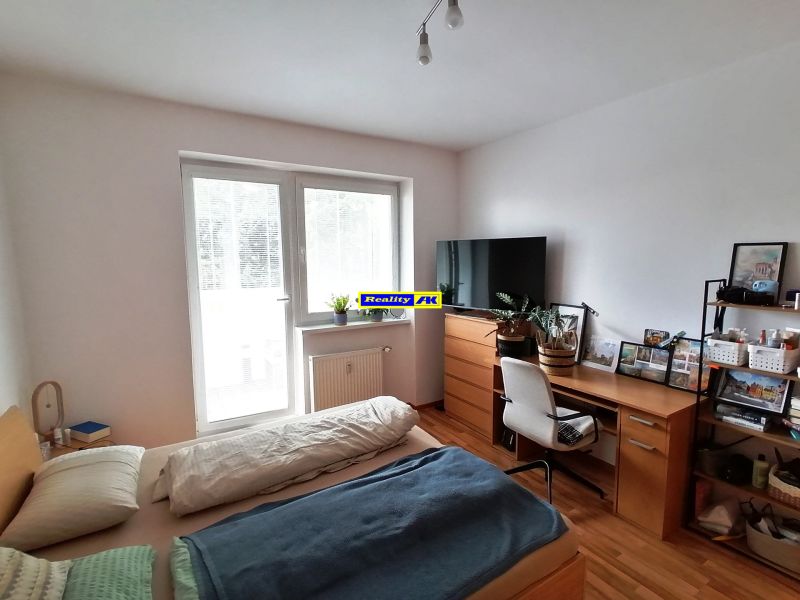 Bedroom area in a studio apartment with wood-patterned flooring and a desk.