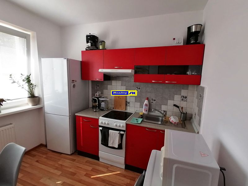 A kitchen with red cabinets and a wood-patterned floor in a studio apartment.