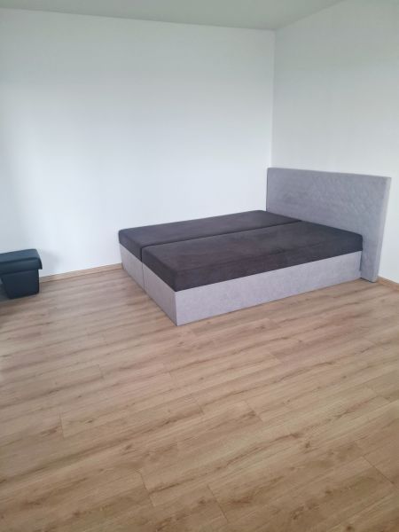A bedroom in a studio apartment with a bed and a wooden-patterned floor.