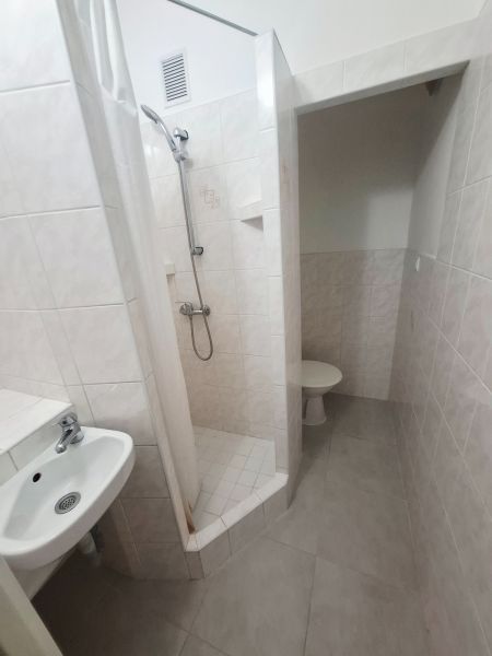 A bathroom with a sink, shower, and toilet in light tile colors, studio apartment.