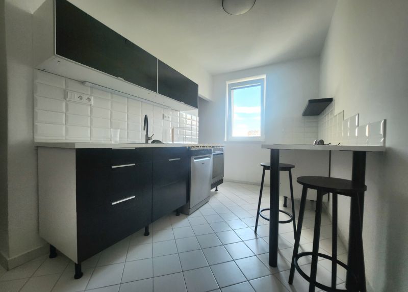 A kitchen in a 3-room apartment with white tiles and dark cabinets.