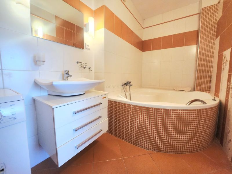 A bathroom with a corner bathtub, sink, and washing machine in a 3-room apartment.