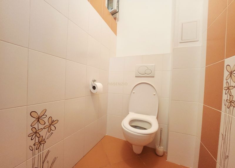 A toilet with white tiles and orange flooring in a 3-room apartment.