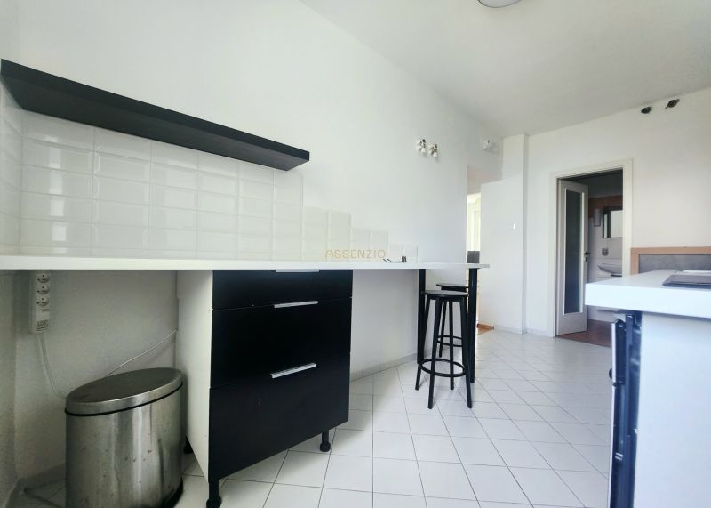 A kitchen with white tiles, black furniture, and a bar stool in a 3-room apartment.