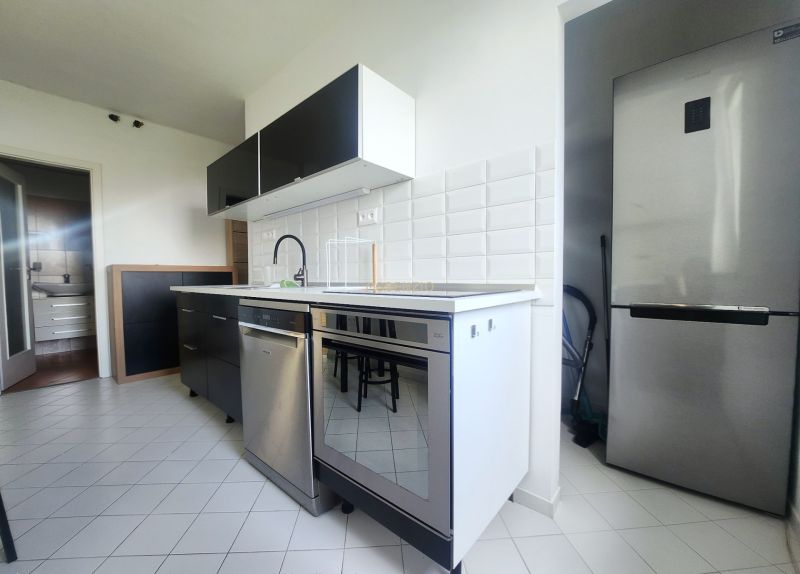 A kitchen with white tiles, a stainless steel dishwasher, and a refrigerator in a 3-room apartment.
