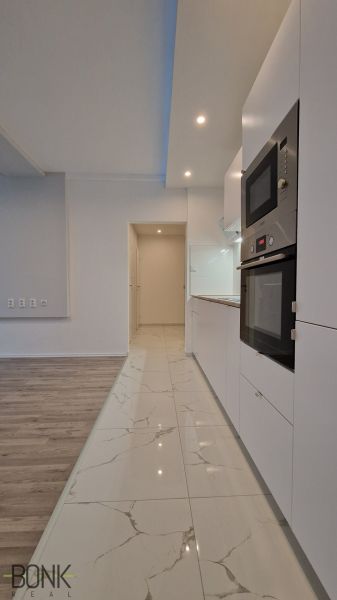 A kitchen with white cabinets and appliances in a 2-room apartment, flooring with a wood decor.