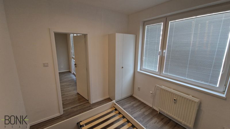A bedroom in a 2-room apartment with white walls and a wooden decor floor.