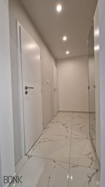 A hallway in a 2-room apartment with white doors and shiny marble tiles.