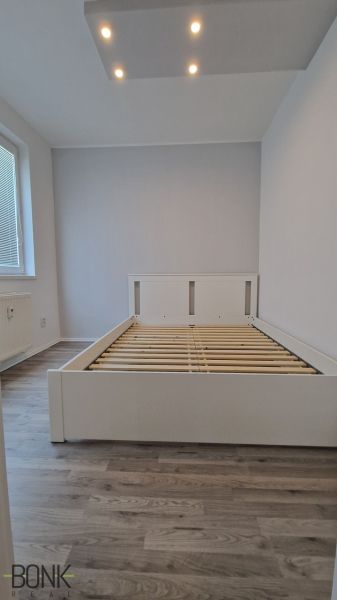 A double bed in a room with wood-patterned flooring and ceiling lighting.