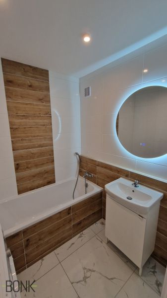 Bathroom with a mirror and a bathtub, walls with wood decor, in a 2-room apartment.