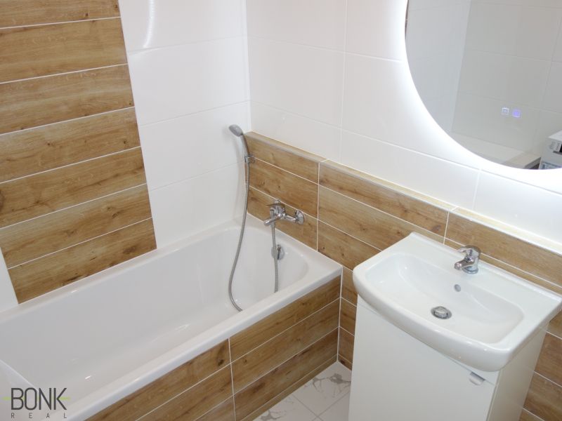 A bathroom with a bathtub and tiles with a wooden decor in a 2-room apartment.