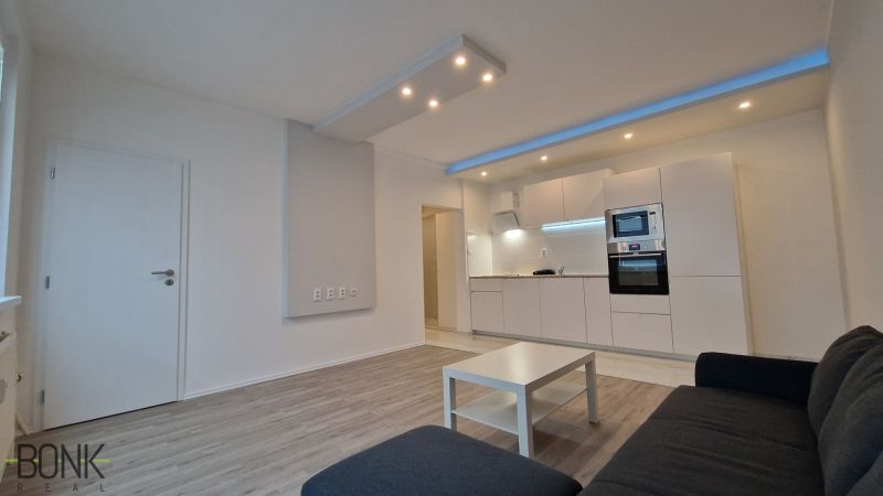 Living room with kitchen in a 2-room apartment, white furniture set, wooden decor flooring.
