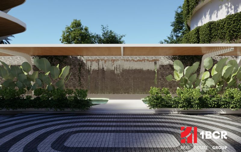 The exterior of an apartment building under construction in Phuket, with foliage and a decorative wall under a canopy.