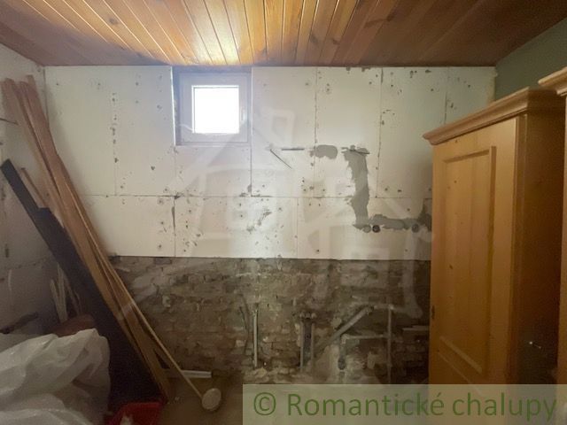 A room with a wooden ceiling, a brick wall, and old furniture in a family house.
