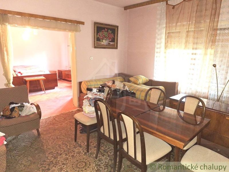 Living room of a family house with a wooden table and a sofa, adjacent room with a bed.