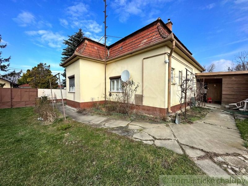 A family house in Kolárovo with a garden, paving, and a satellite dish on a yellow facade.