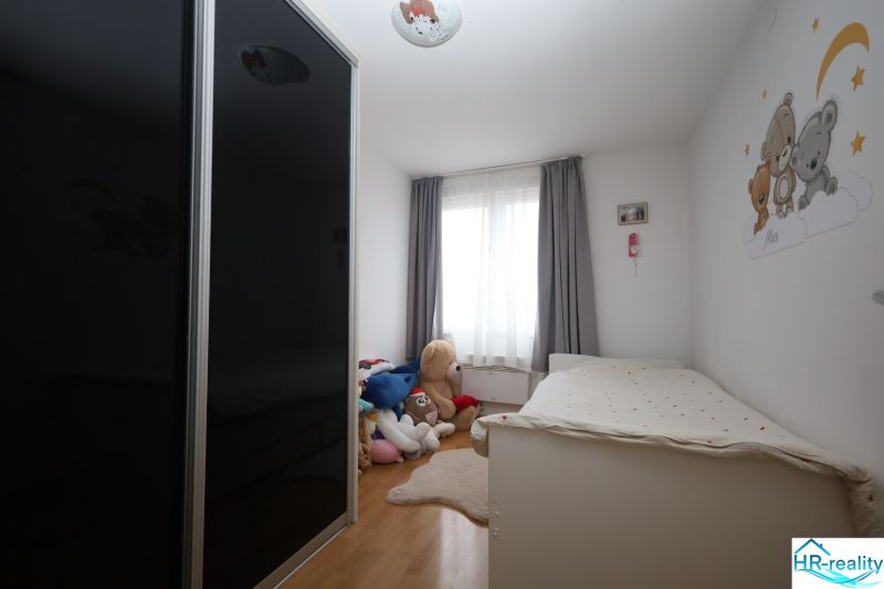 Children's room in a recreational apartment with a bed, wardrobe, and plush toys on the floor with wooden decor.