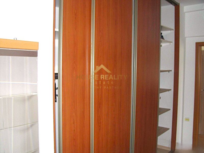 A built-in wardrobe with a wooden decor in a 2-room apartment, complemented by white walls and shelves.