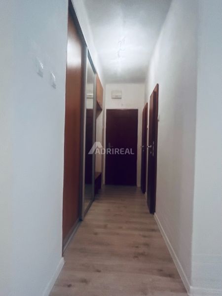 A narrow hallway in a 3-room apartment with a wooden decor floor and a built-in wardrobe.