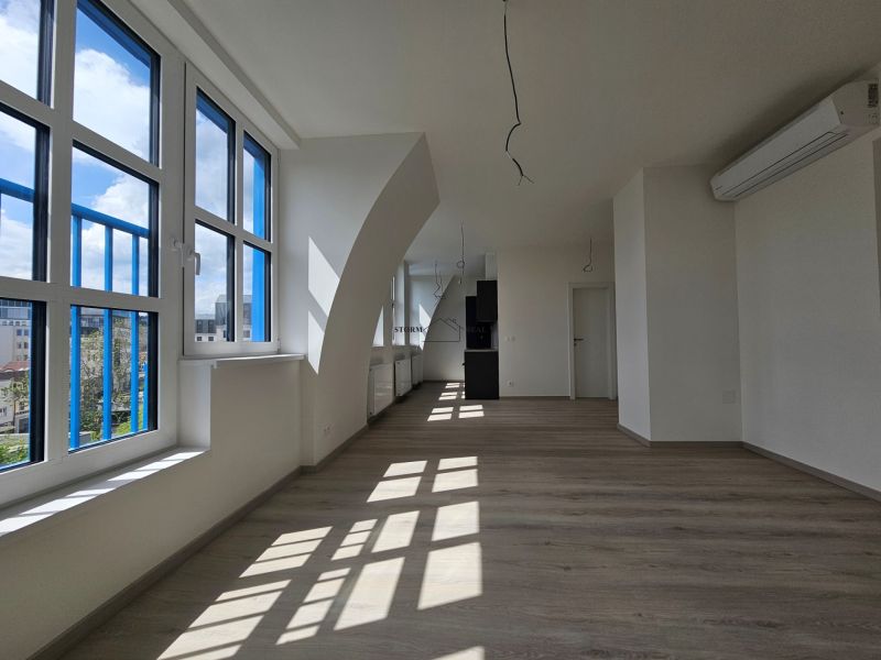 A spacious room with large windows, wooden decor flooring in a studio apartment.