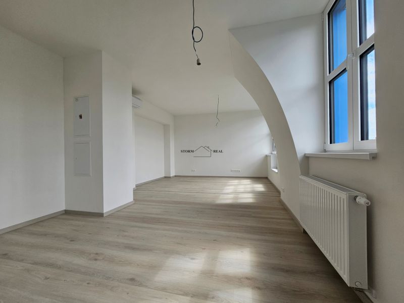 Spacious living room with wood-patterned flooring and large windows in a studio apartment.