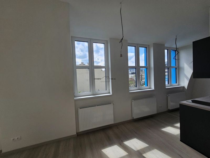 A bright room with three windows and a wooden decor floor in a studio apartment.