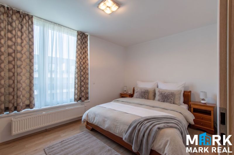 Bedroom with a large window, double bed, and wooden decor flooring in a 2-room apartment.