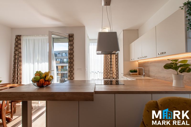 A kitchen in a 2-room apartment with an open balcony and wooden floor decor.