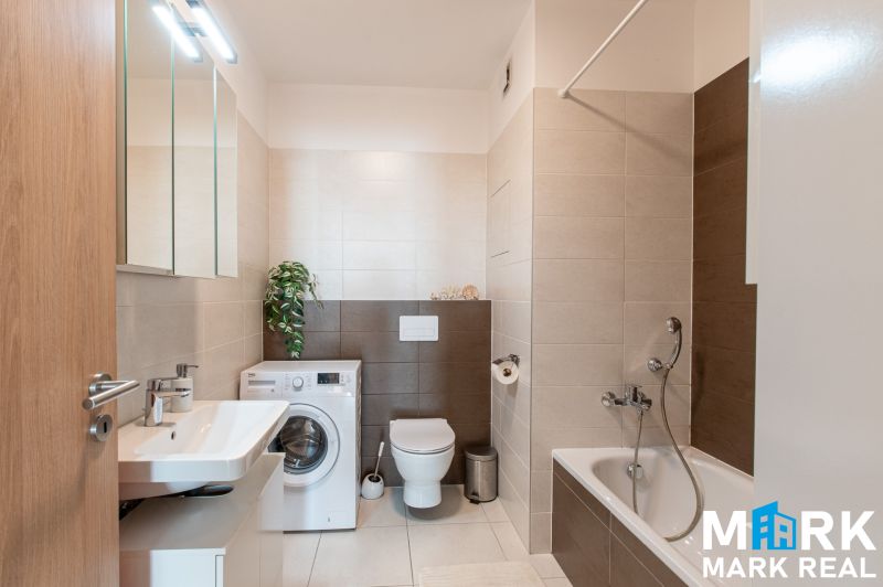 Bathroom with a bathtub, washing machine, and sink in a 2-room apartment.