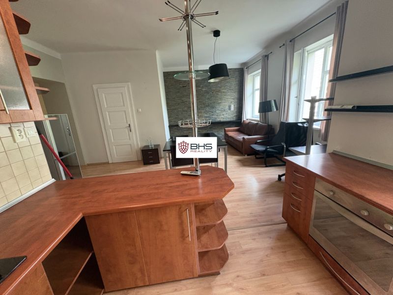 Living area in a two-room apartment with a wood-patterned floor and a kitchenette.