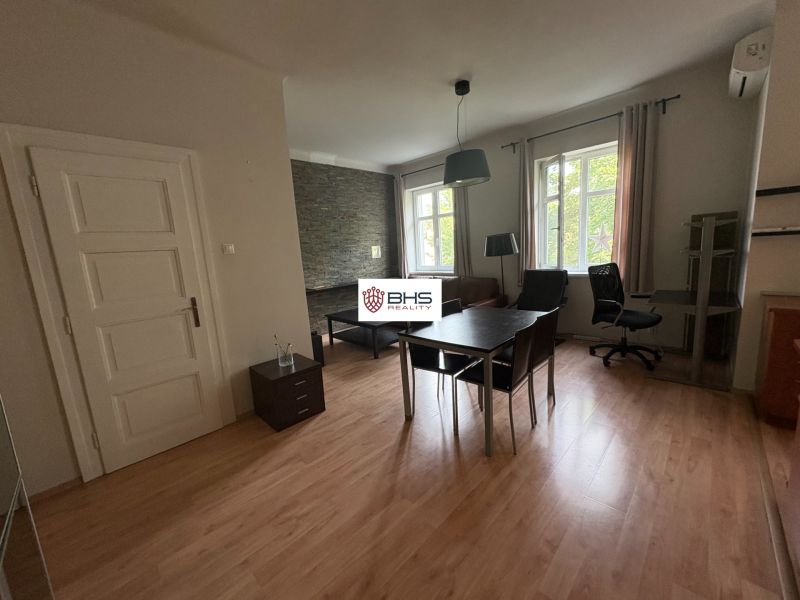 Interior of a 2-room apartment with a wooden decor floor, table, and chair.