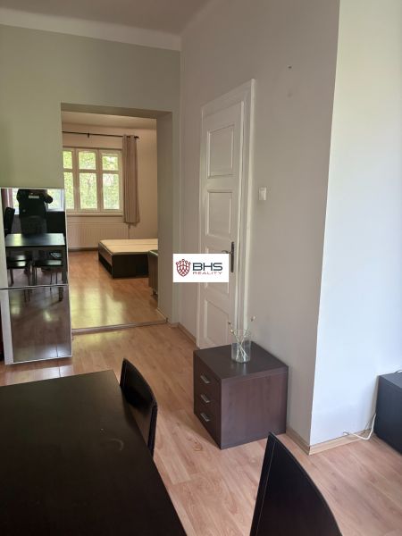Interior of a 2-room apartment with a wooden decor floor, seating area, and entrance to the bedroom.