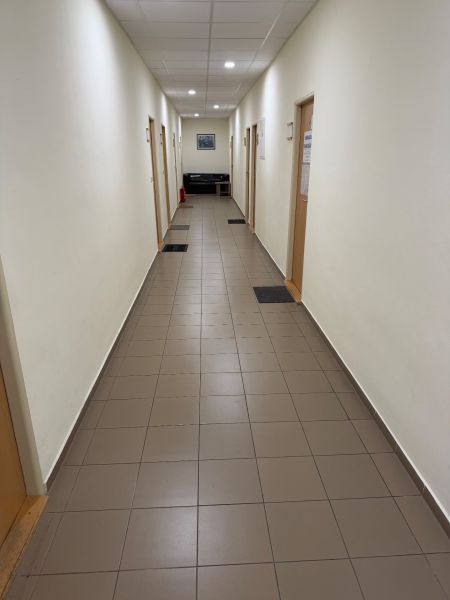 A narrow hallway in offices with tiles, doors, and a sofa at the end.