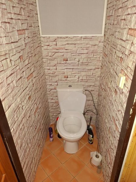 A bathroom with a toilet and walls with a brick wall decor in a 2-room apartment.