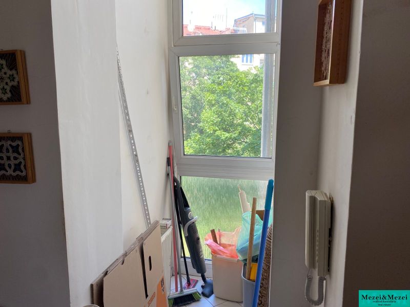 The window section of a 2-room apartment with cardboard boxes, cleaning supplies, and an intercom.