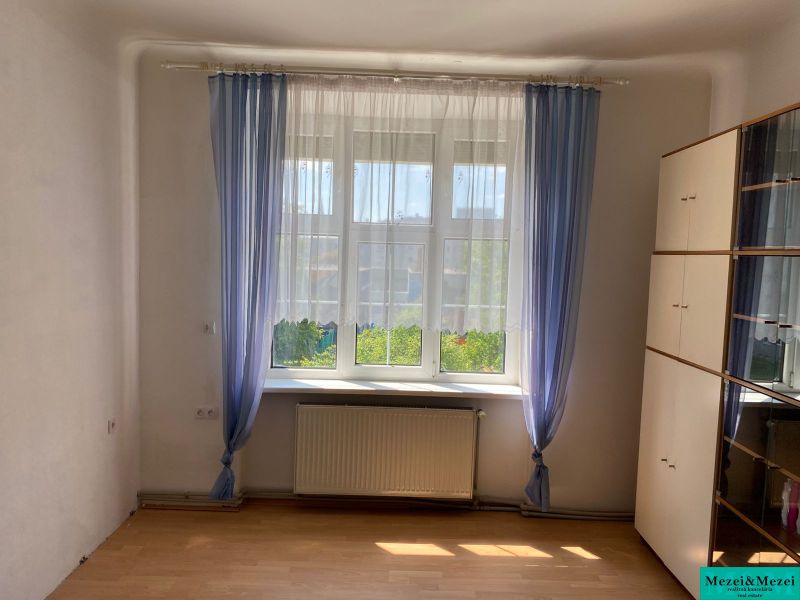 A room with a cabinet, a window, and curtains in a 2-room apartment, with a wooden decor floor.