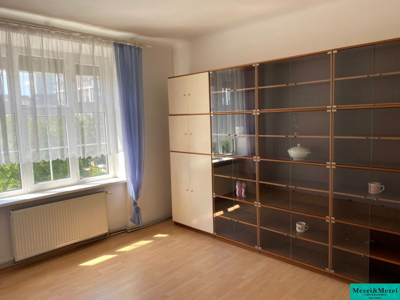 Living room in a 2-room apartment with a window, curtains, and a cabinet with shelves.