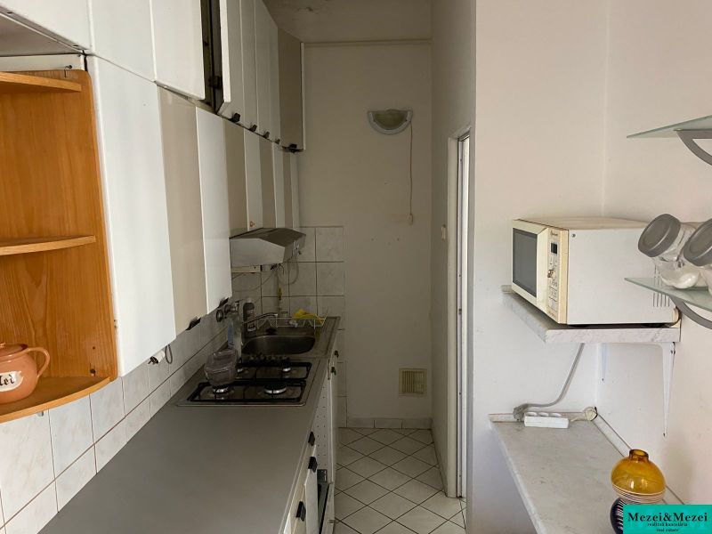 A narrow kitchen in a 2-room apartment with white furniture and tiles.