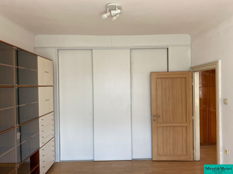 Interior of a 2-room apartment with a white wardrobe and shelving unit, floor with wood decor.