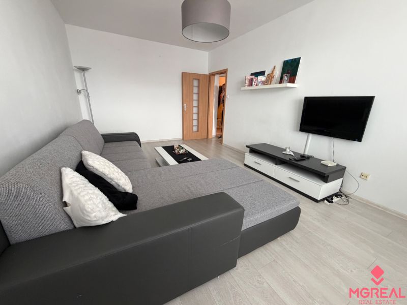 Living room in a two-room apartment with a wooden decor floor and a corner sofa.
