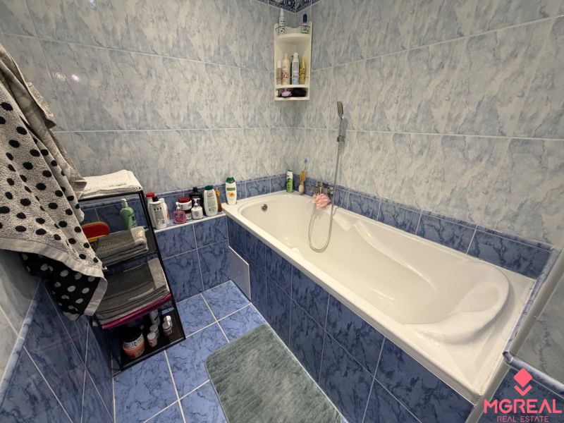 A bathroom with a bathtub and blue tiles in a 2-room apartment.