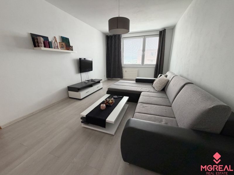 Living room in a two-room apartment with a wooden decor floor and a gray sofa.