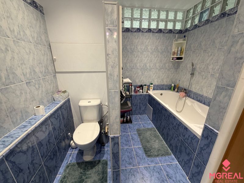 A bathroom in a 2-room apartment with a bathtub and blue tiles.