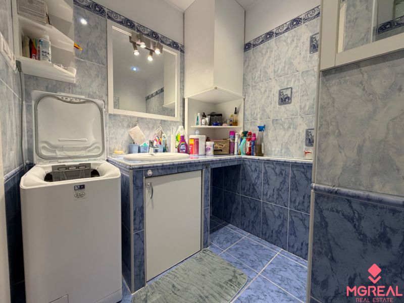 A bathroom in a 2-room apartment with a washing machine and blue tiles.