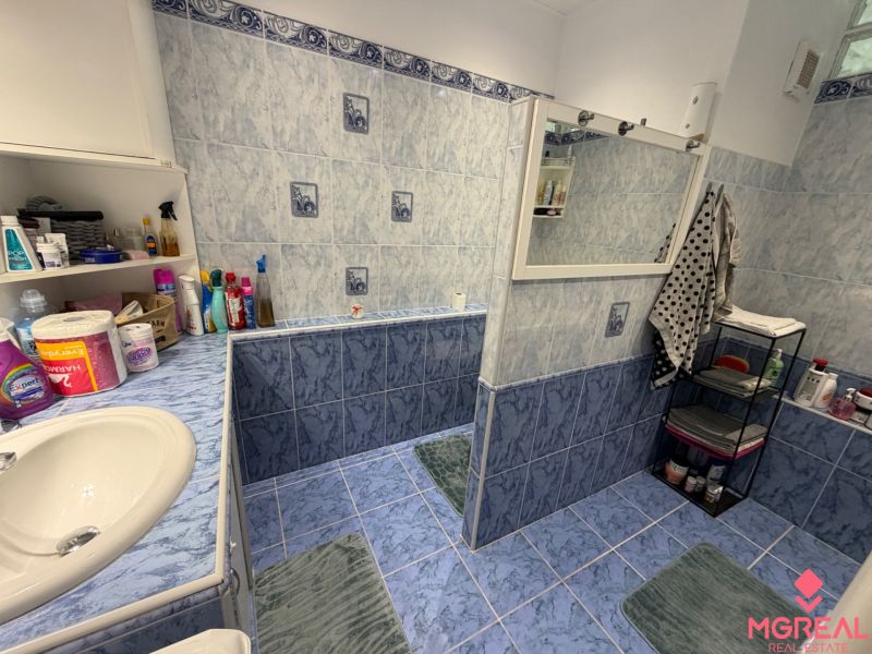A bathroom with blue tiles and a shelf in a 2-room apartment with toiletries.