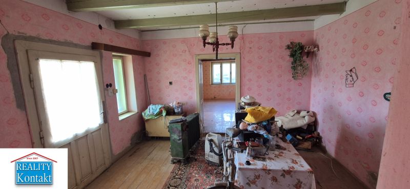 A room in a family house with older furniture, pink wallpaper, and wooden flooring.
