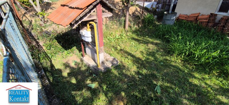 The garden of a family house in Dedinka with a lawn, a gas meter, and a pile of soil in the background.
