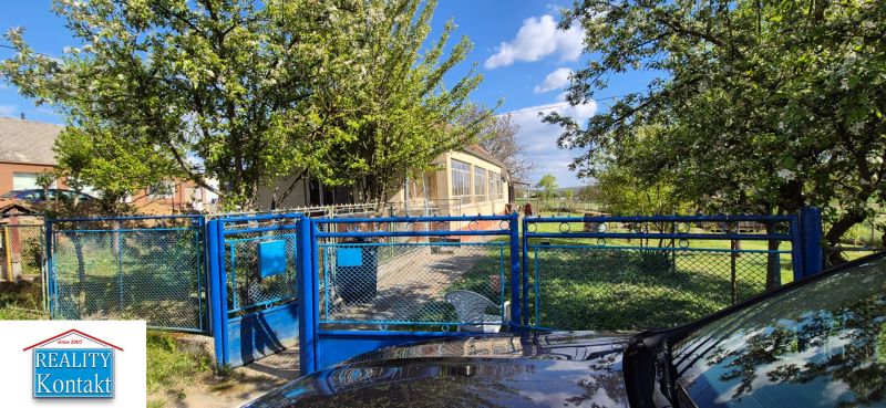 A family house in Dedinka with a blue gate and a garden full of greenery.