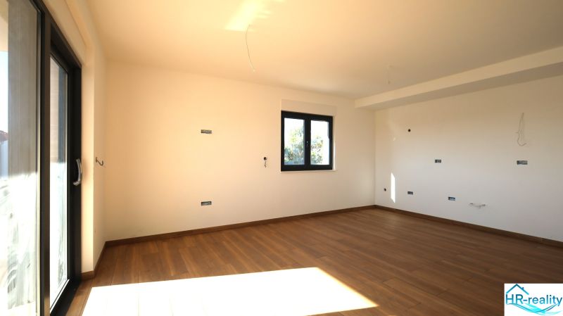 A spacious room with a large window and a wooden decor floor in a Holiday Apartment.