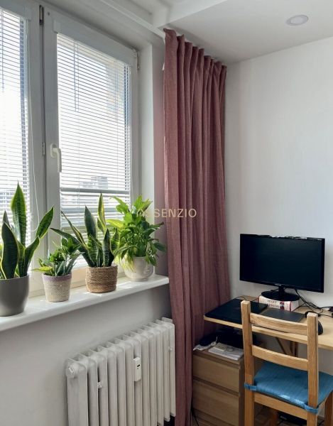 A room with a table, monitor, plants on the windowsill, and a burgundy curtain in a 2-room apartment.